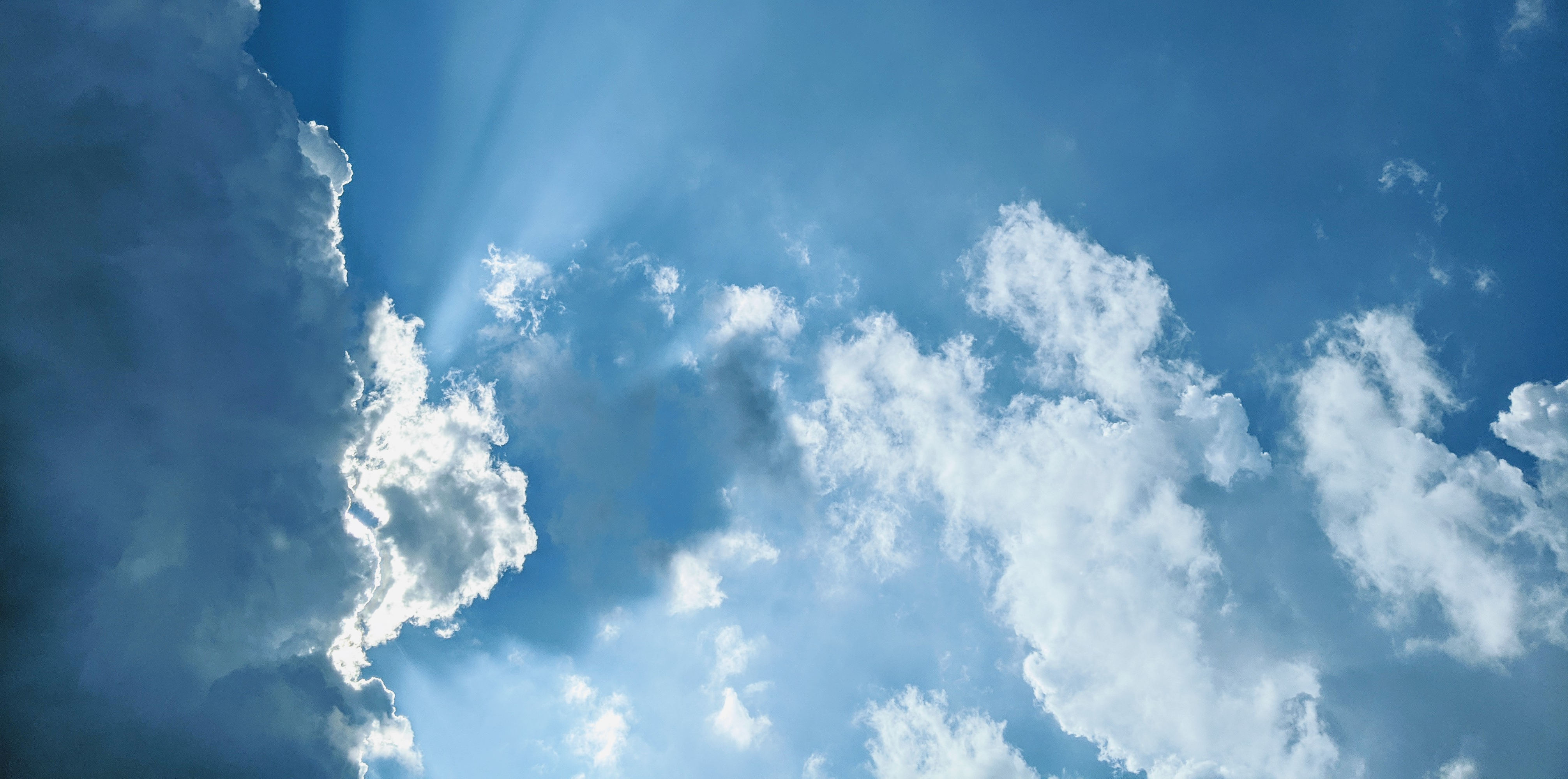 Sun shining through clouds with blue sky in the background.